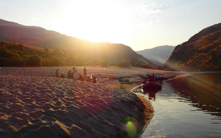 a watercraft rests on a calm river while the sun sets over mountains in the background